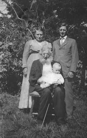 Andrew Bohl seated in the pasture with baby in arms and son and granson behind the chair.